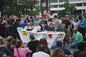 Τραπεζάκι συνειδητοποίησης των «Αγανακτισμένων» και κατανόησης των «βλαβερών συνεπειών του μνημονίου», το καλοκαίρι του 2011, στην πλατεία Συντάγματος. Από τους πέντε ομιλητές (από αριστερά: ένας άγνωστος, Καζάκης, Κατρούγκαλος, Τσακαλώτος, Βαρουφάκης), οι τρεις τελευταίοι είναι υπουργοί της κυβέρνησης Τσίπρα.